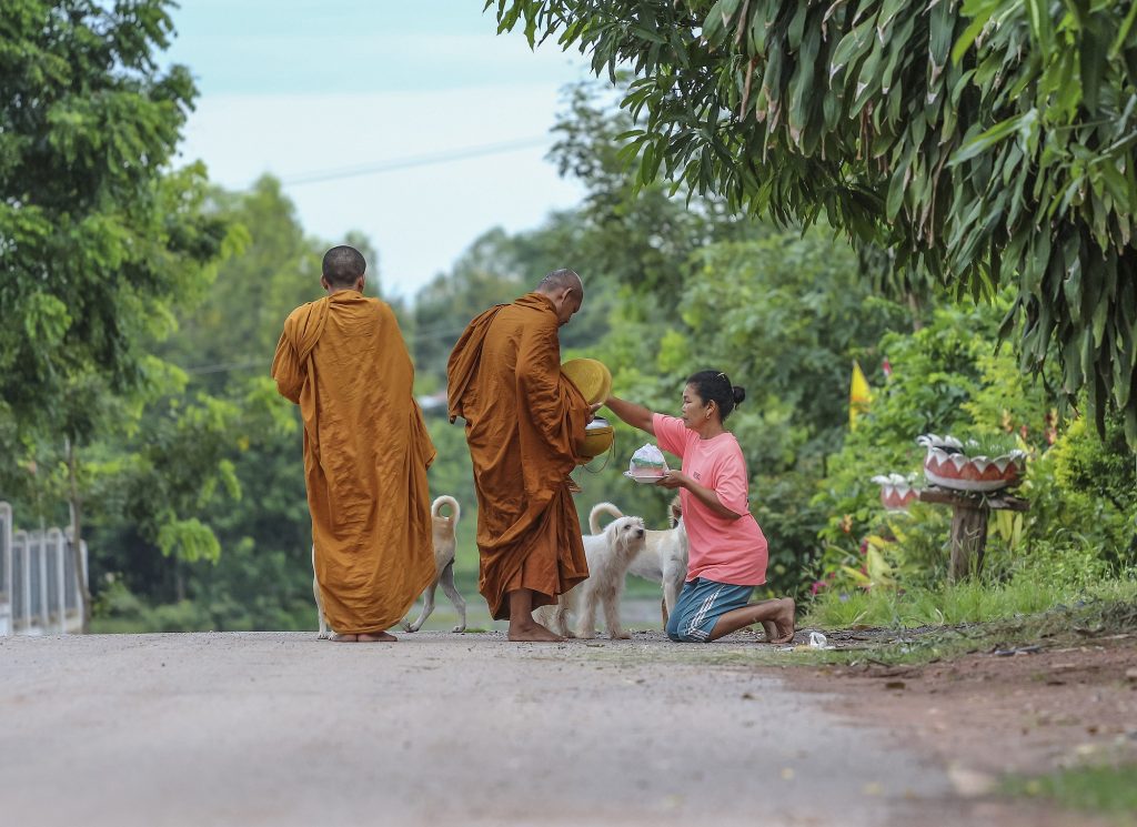 Woman making merit by giving offerings to monks in Thailand